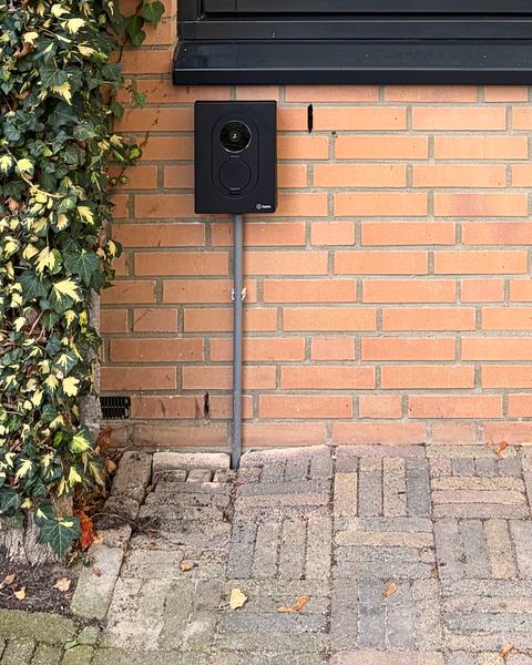 Zwarte Zaptec Go 2 laadpaal op een rode bakstenen gevel naast klimop, met de kabel in een grijze buis