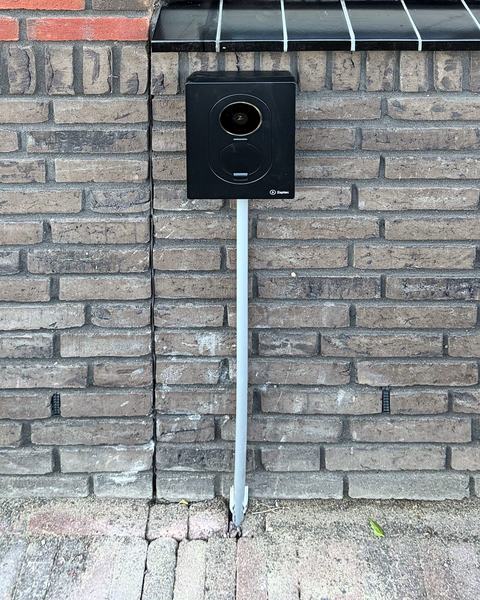 Zwarte Zaptec Go 2 laadpaal op een bakstenen gevel onder een raam, met de kabel in een grijze buis naar de grond